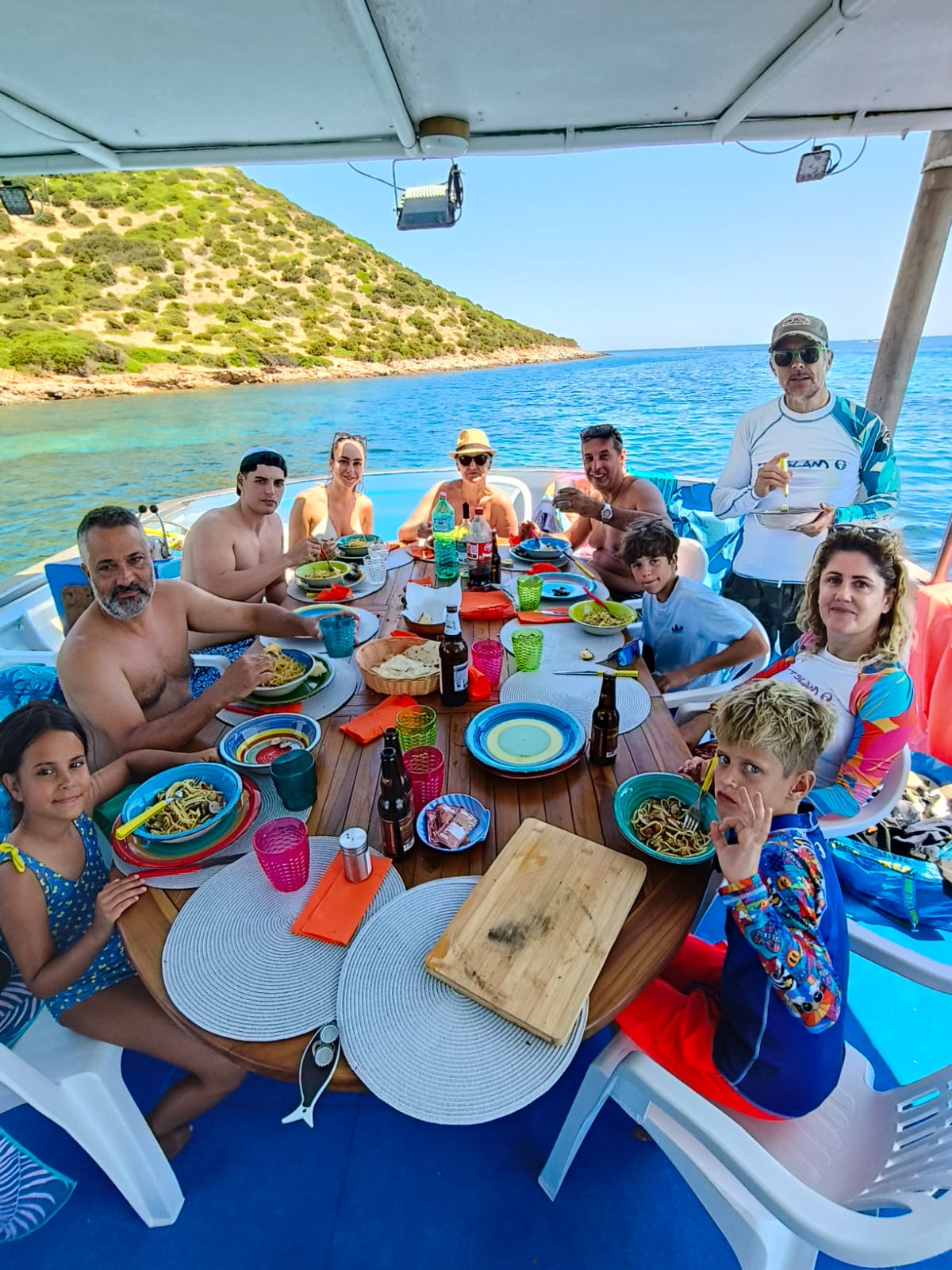 Ospiti a tavola sulla barca gustano spaghetti al pescato fresco davanti al mare di Teulada